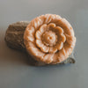 A round handmade soap with a floral pattern, predominantly pink to orange in color, displayed on a grey stone.
