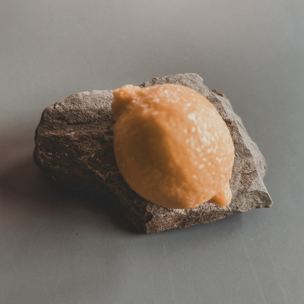 A bar of handmade soap designed to resemble a lemon, placed on a textured grey surface.