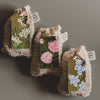 Three small woven bags with floral tags on a gray background