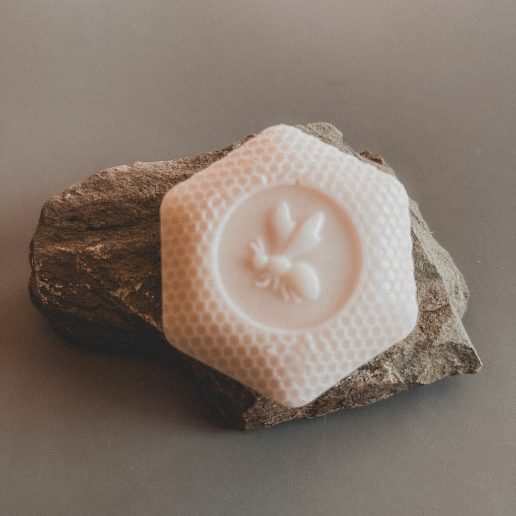 A handmade soap bar with a floral pattern, predominantly white, displayed on a textured grey surface.