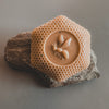 A bar of soap with a honeycomb pattern and a poppy seed design in the center, placed on a stone surface.