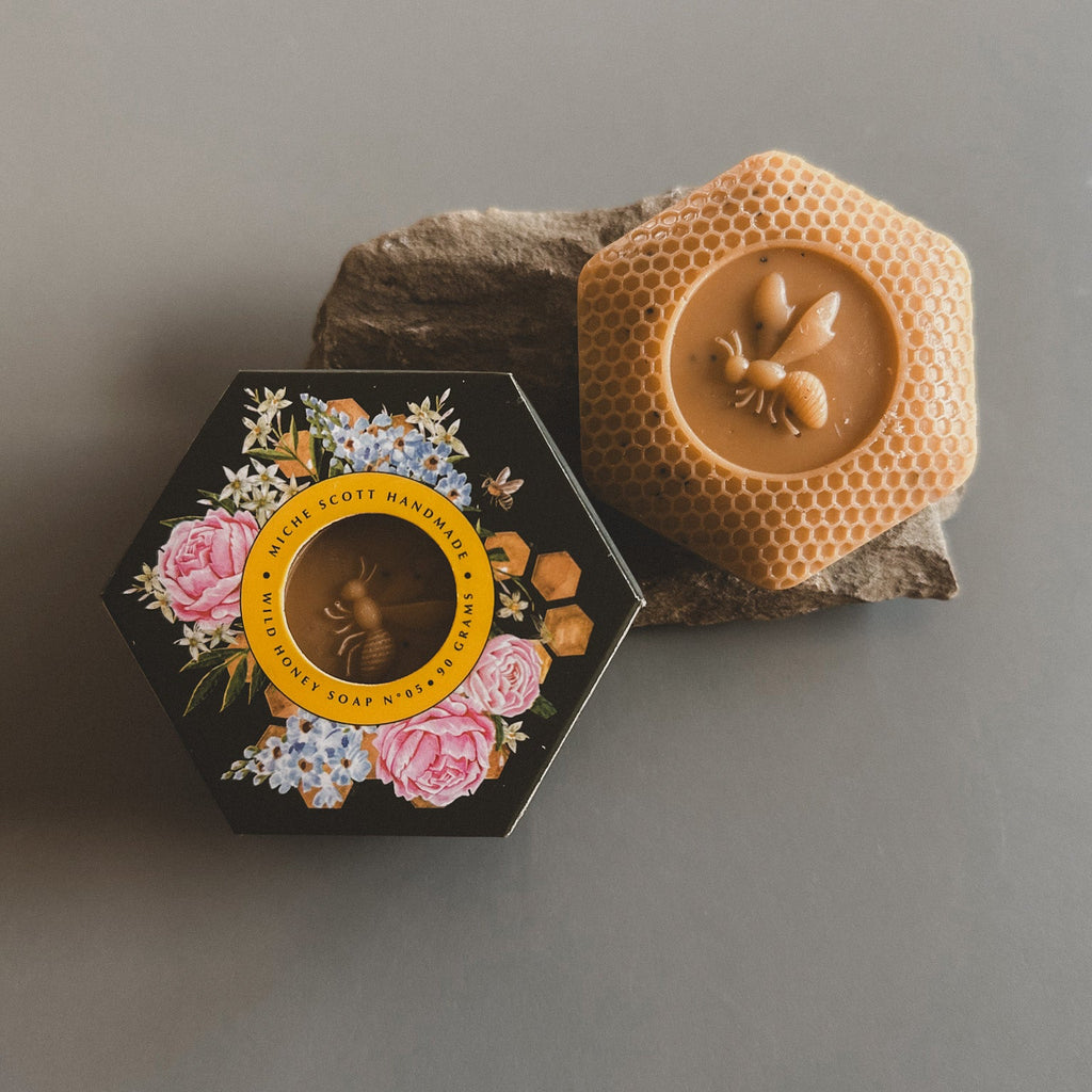 Hexagonal black box with floral design and bee emblem, next to a honeycomb-shaped product on a gray background
