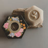 Hexagonal soap packaging with floral design and bee emblem on a gray background