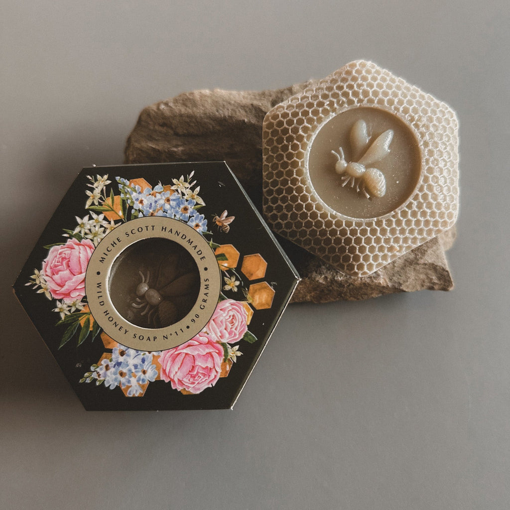 Hexagonal soap packaging with floral design and bee emblem on a gray background
