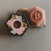 Hexagonal soap with floral design and bee emblem on a gray background